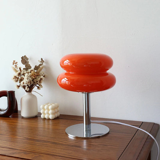 Modern table lamp with a vibrant orange glass shade, sitting on a wooden surface alongside minimalist vases and decor, adding a pop of color and a contemporary touch to the space.