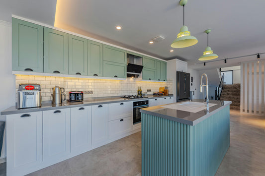 Modern kitchen with under-cabinet lighting, mint green cabinets, and a large island featuring a sleek faucet, creating a bright and functional cooking space.