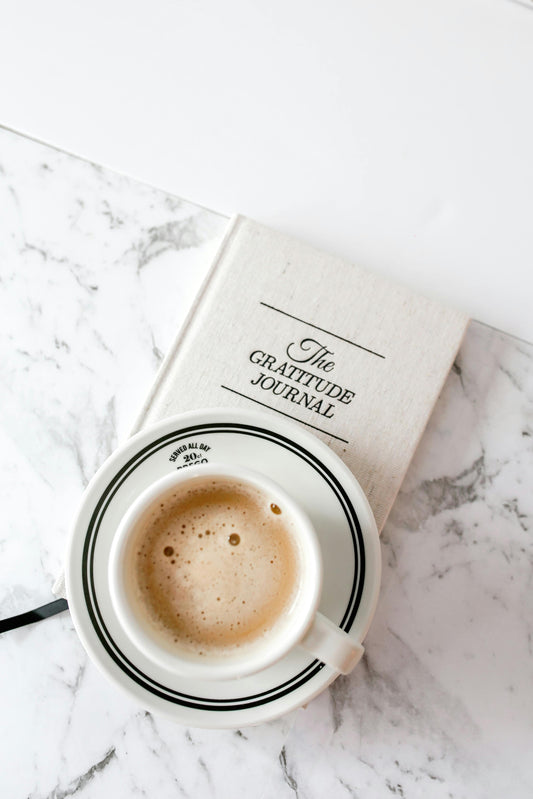 A gratitude journal resting on a marble surface with a cup of coffee on top.