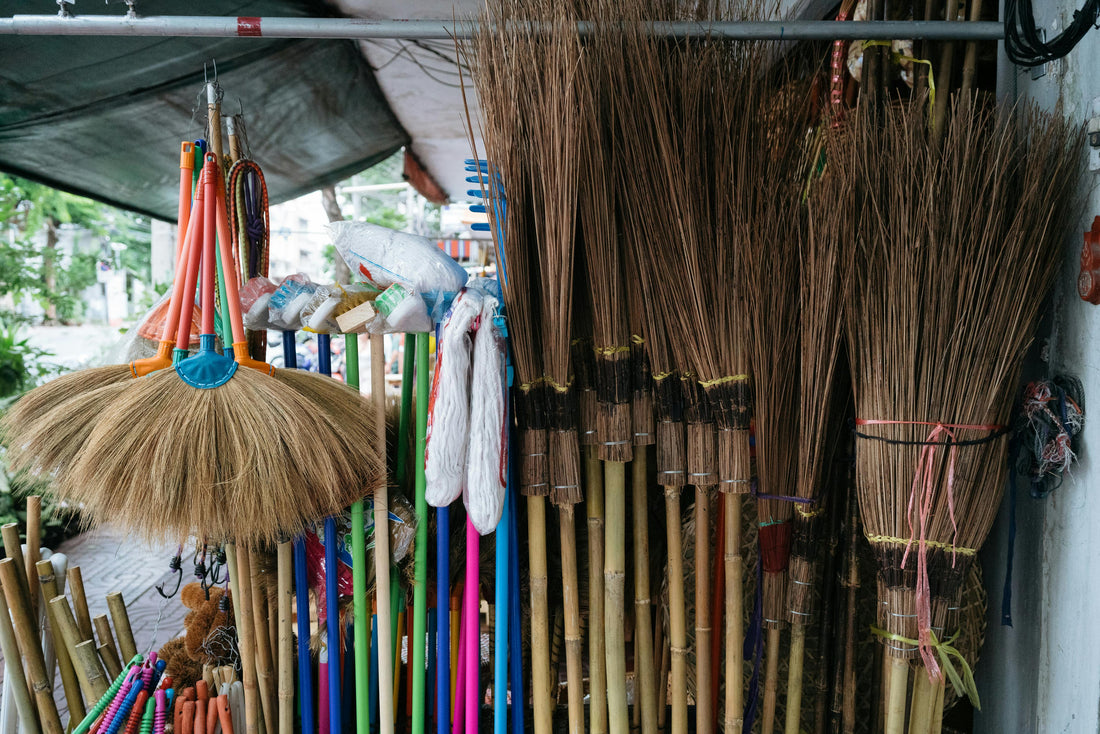 Outdoor market display featuring eco-friendly brooms made from bamboo and natural straw, offering a sustainable and rustic touch to household cleaning tools.