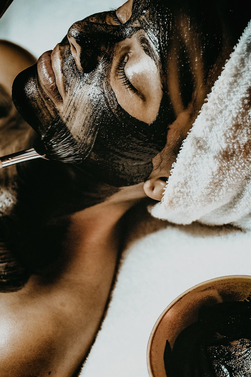 Person receiving a black facial mask treatment, lying with eyes closed, creating a relaxed and calming atmosphere.